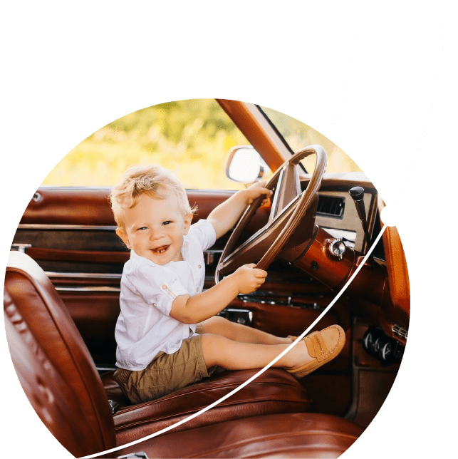 Young child sitting in the front seat of a parked classic car