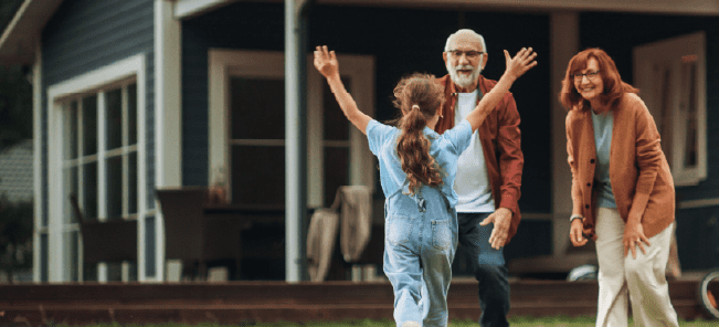 Child running to grandparents in front of large house.