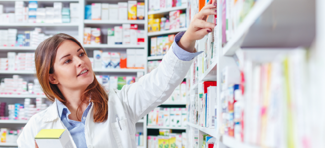 Pharmacy worker looking through various pill bottles in pharmacy area.