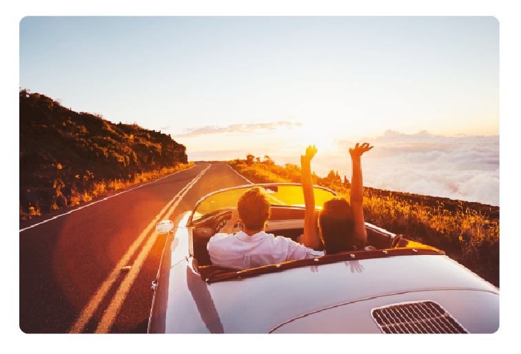 Classic car driving down a road over looking a cliff, the passenger has their hands in the air