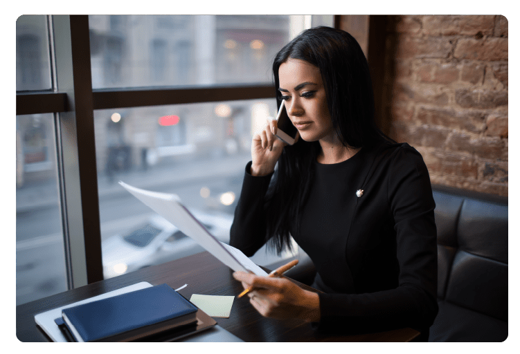 Young caucasian woman prosperous business worker holding paper document with monthly revenue report and talking with partner via cell telephone while sitting in restaurant. Manager reading resume