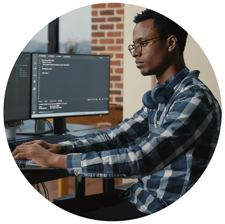 Programer thinking while touching beard and fixing glasses while typing on laptop sitting at desk