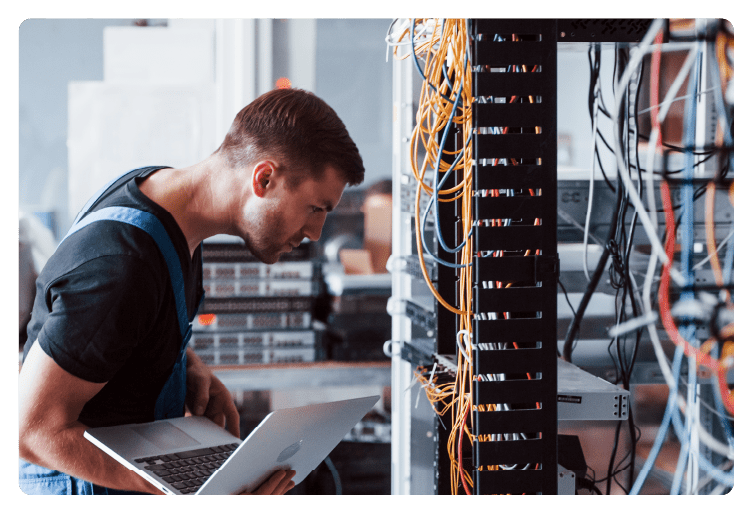 Young man in uniform and with laptop works with internet equipment and wires in server room