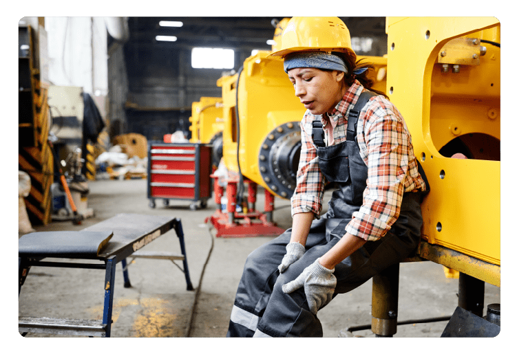 Young female worker of warehouse touching hurting knee while sitting by machine