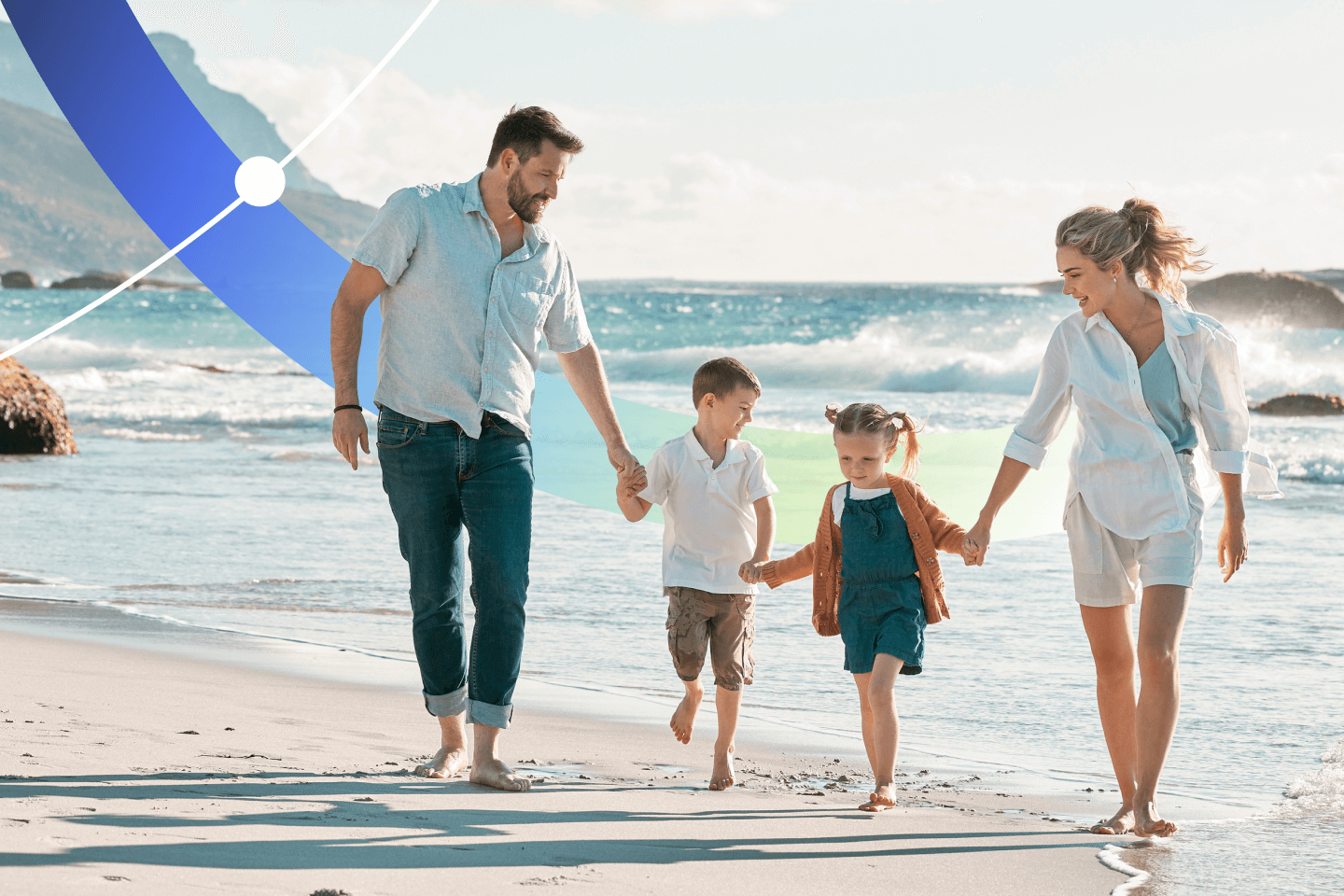 Family of four walking barefoot along a sandy beach with waves in the background, holding hands and smiling together.